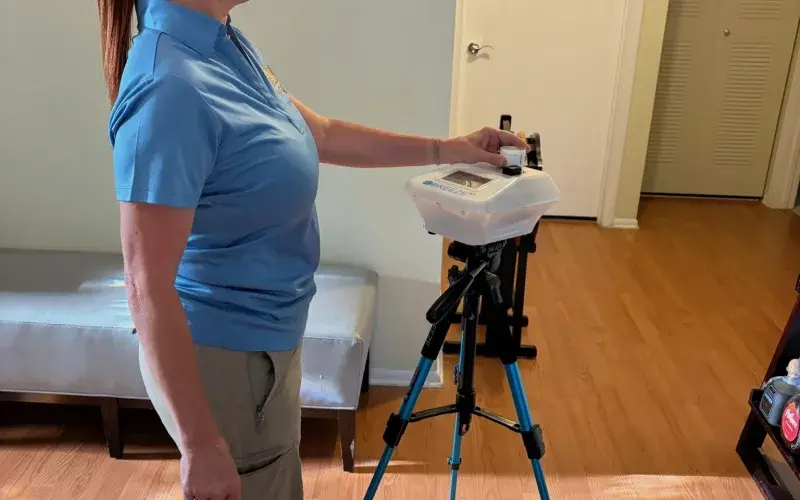 Inspector running an indoor air sampling pump mounted on a tripod in a living room